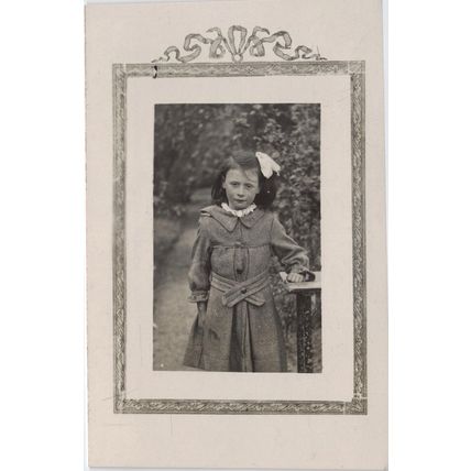 Vintage postcard young girl in a garden. Buttoned coat, hair ribbon
