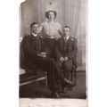 Postcard Unknown WOMAN STANDING, TWO MEN SITTIN...